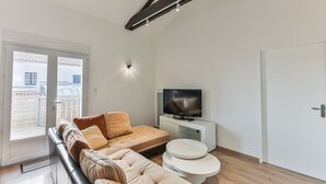 Ein modernes Wohnzimmer mit einem Ecksofa, einem Flachbildfernseher und einem kleinen runden Tisch.