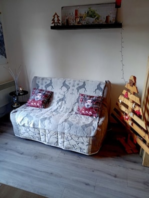 Ein gemütliches Wohnzimmer mit einer Couch, einem kleinen Tisch mit einer Dekoration und einem Wandregal mit einem Gemälde.