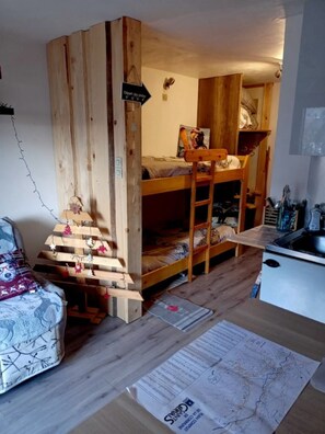Habitación compacta con literas, una kitchenette pequeña y una decoración de madera en la pared.