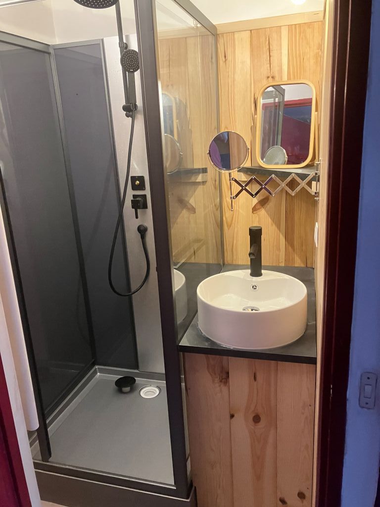 A bathroom with a glass-enclosed shower, a round sink with a mirror, and wooden paneling.