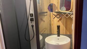 A bathroom with a glass-enclosed shower, a round sink with a mirror, and wooden paneling.