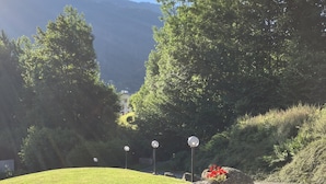 A landscaped area with a paved path, wooden planters with flowers, and a backdrop of trees and hills.