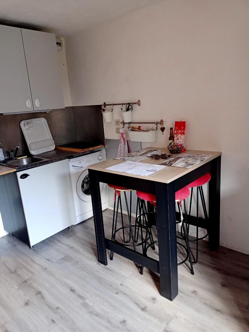 Eine kleine Küche mit Waschmaschine, einem Esstisch mit Hocker und einer Wäscheleine.