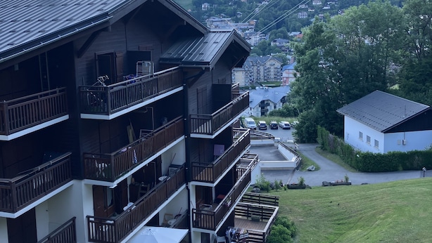 A multi-story building with balconies, a ski lift in the background, and a mountainous landscape.