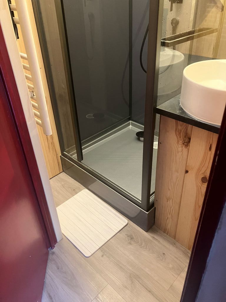 Une salle de bain avec une douche à parois de verre, un meuble-lavabo en bois et un petit tapis sur le sol.