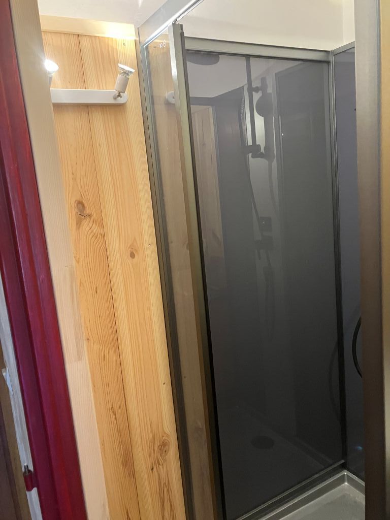 Una habitación con pared de paneles de madera, puerta de vidrio y estante blanco.