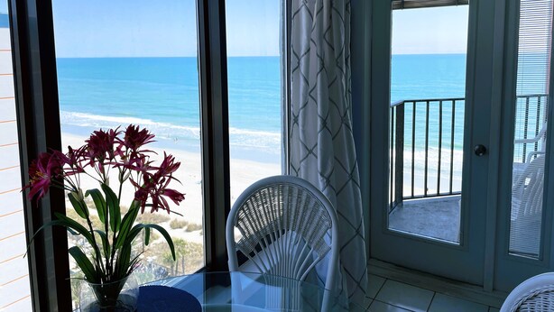 A room with a view of the beach, a chair, a potted plant, and a door leading to an outdoor area.