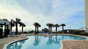 A swimming pool with blue lounge chairs and palm trees, surrounded by a brick patio.