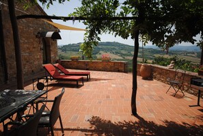 A patio with red lounge chairs, a table, and a view of rolling hills.