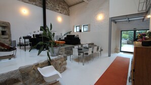 Un intérieur moderne avec un mur en pierre, un comptoir d’accueil, un espace détente avec des chaises blanches et une grande fenêtre.