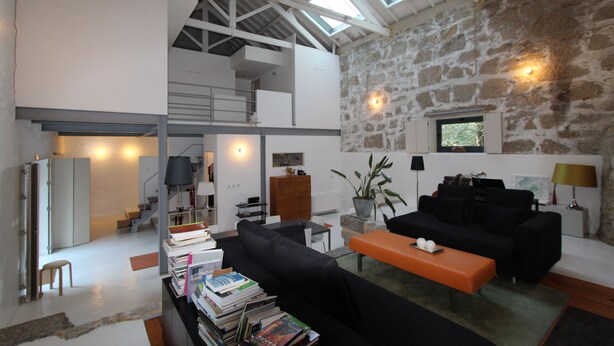 Un vaste espace de vie doté d’un haut plafond, de murs en pierre et d’un canapé noir moderne.