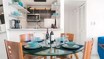 Una cocina moderna con electrodomésticos integrados, un comedor con mesa de vidrio y sillas azules, y una puerta blanca al fondo.