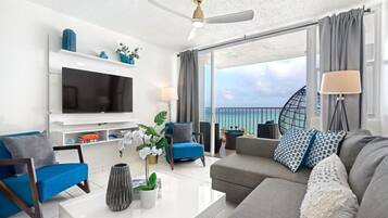 Un soggiorno moderno con una TV a schermo piatto, sedute confortevoli, un tavolino da caffè e vista sull'oceano.