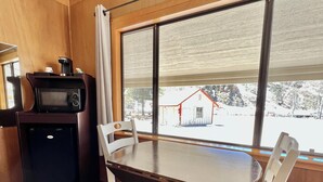 A room with a wooden interior, a dining table with four chairs, a microwave, and a window with a view of a snowy landscape. - Willow Springs Resort (Bridgeport)