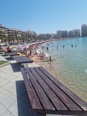 Une plage avec des bancs en bois, une eau claire et des gens qui se baignent.