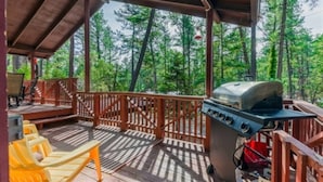 A covered outdoor area with a grill, seating, and a view of a forest.