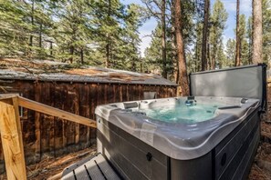 Un jacuzzi en un área boscosa con una terraza de madera y un techo de metal.