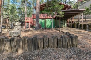 Een rustieke houten chalet met een terras en groene buitenkant, omgeven door een houten omheining en bomen.