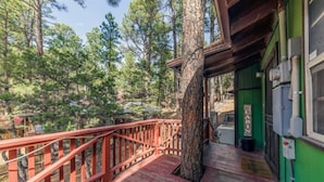 A wooden deck with a red railing, a green building, and a forested background.