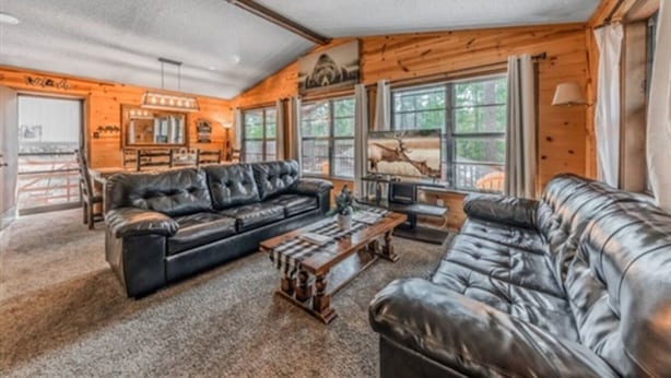A spacious living room with leather sofas, a wooden coffee table, and large windows offering views of the outdoors.