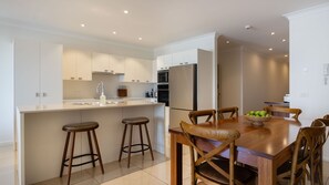 A modern kitchen with a central island, bar stools, a dining table with chairs, and a refrigerator.