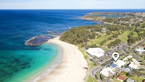 An aerial view of a coastal area with a beach, clear waters, and a residential area with houses and roads. - Beachfront 2 - Steps away from the prestine waters of Mollymook Beach (Mollymook)