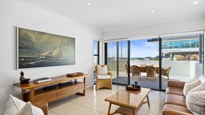 A modern living room with a large painting, a dining area with wicker furniture, and a view of a building across the street.
