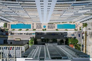 Un edificio alto con dos piscinas, un estacionamiento y vistas a la calle.