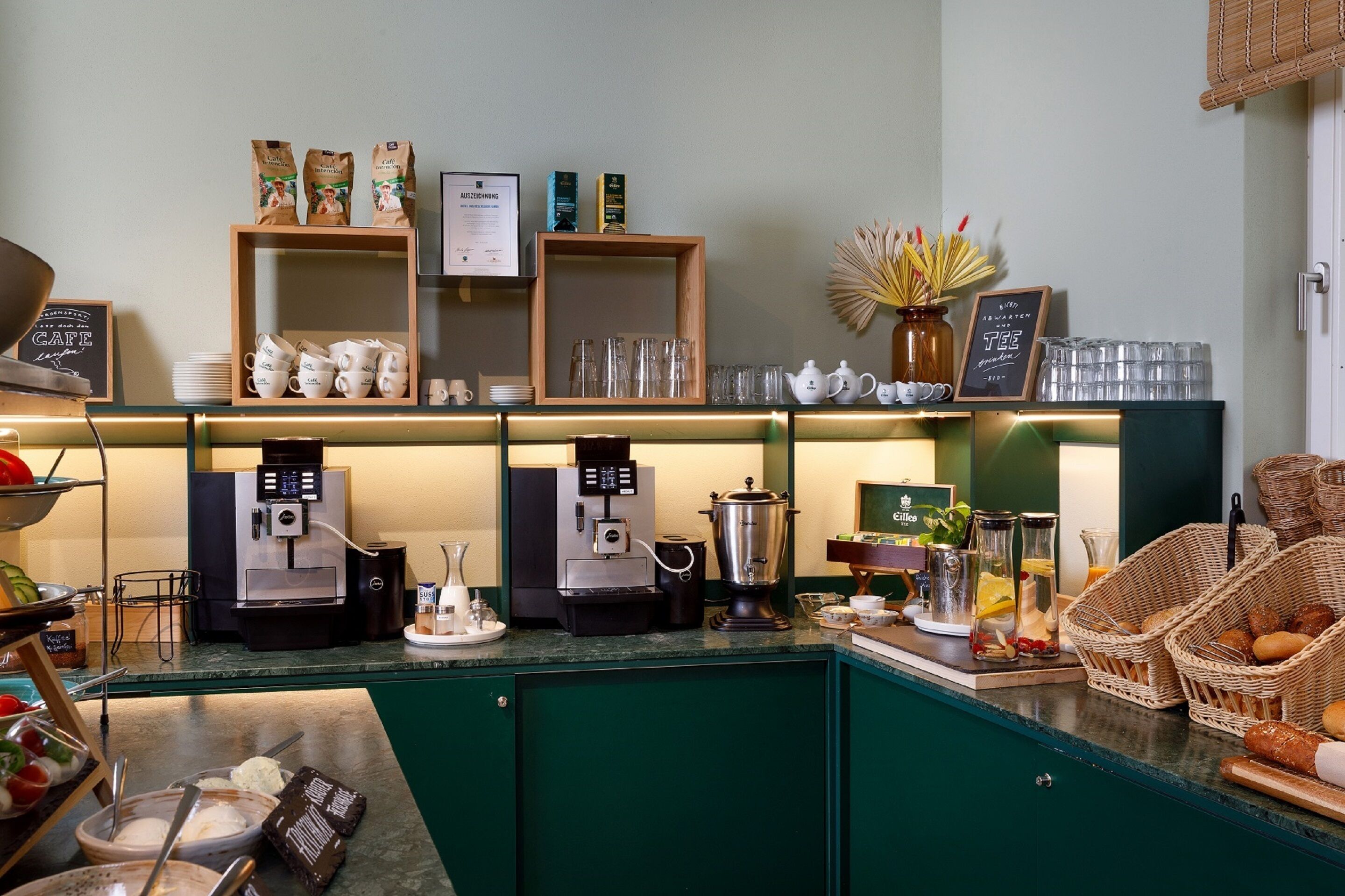 En bardisk i ett kafé med espressomaskiner, koppar och ett varierat utbud av mat och bakverk.