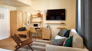 A hotel room with a wooden desk, a chair, a sofa, a TV, and a mirror. - Hotel Das Regensburg (Regensburg)