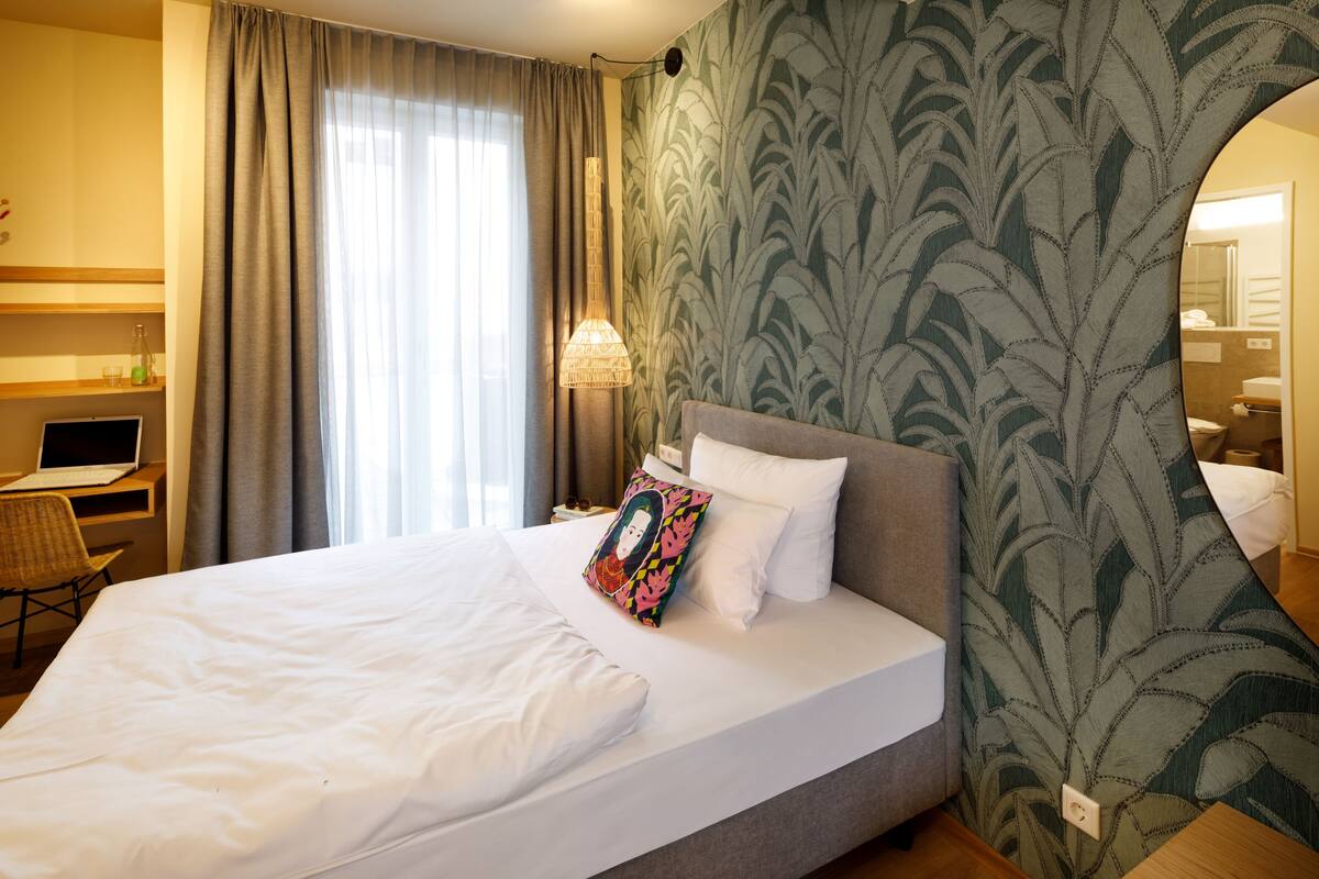Habitación de hotel con una cama grande, un escritorio con una computadora portátil, una silla y un espejo.