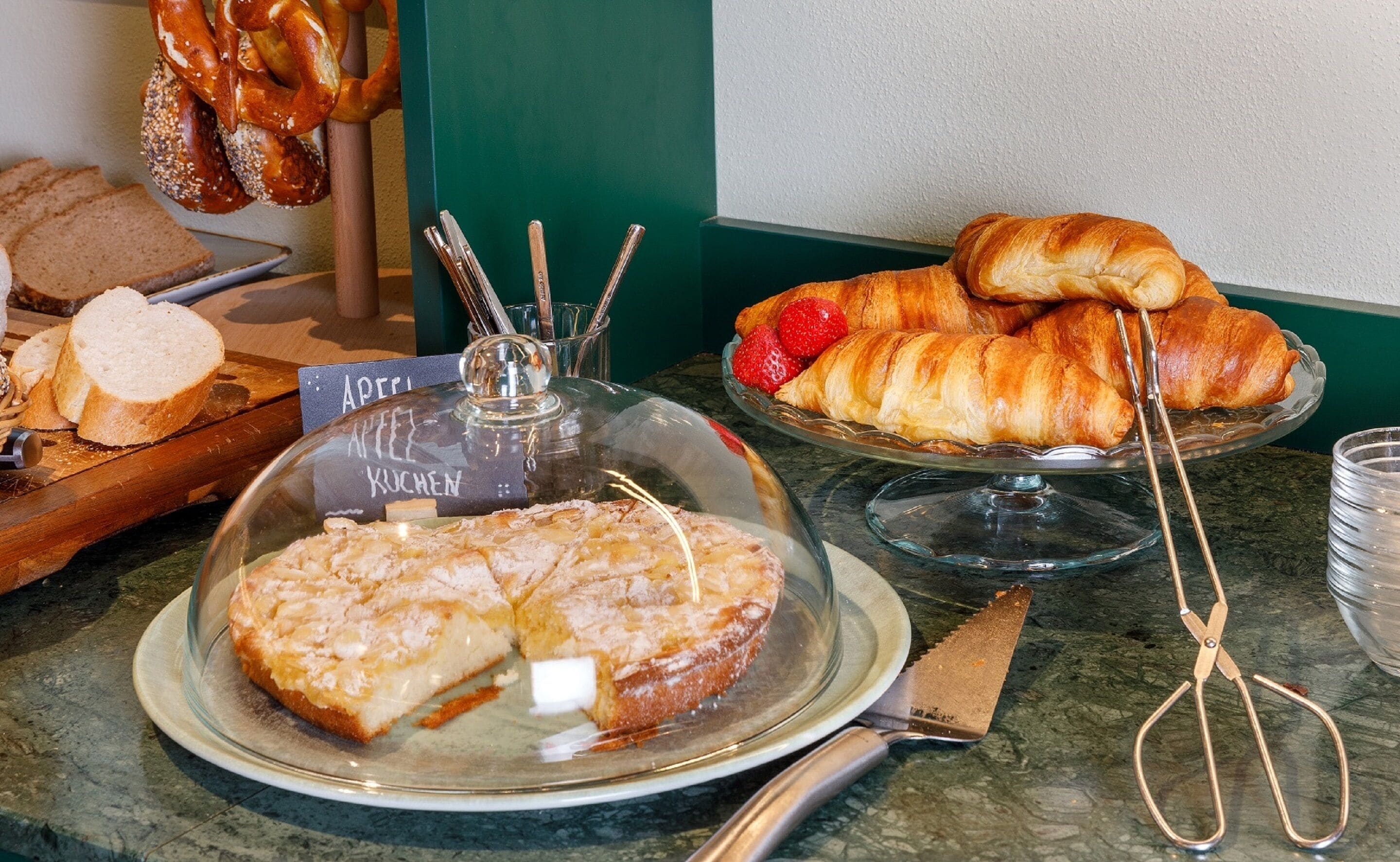 Un bufé con diversas opciones de panadería, incluyendo pan, pasteles y un postre cubierto.