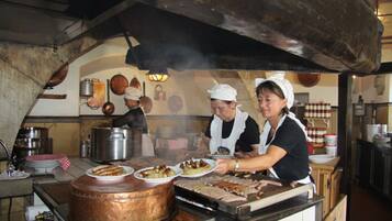 Una cocina con una olla de cobre grande, una parrilla y dos cocineros preparando comida.