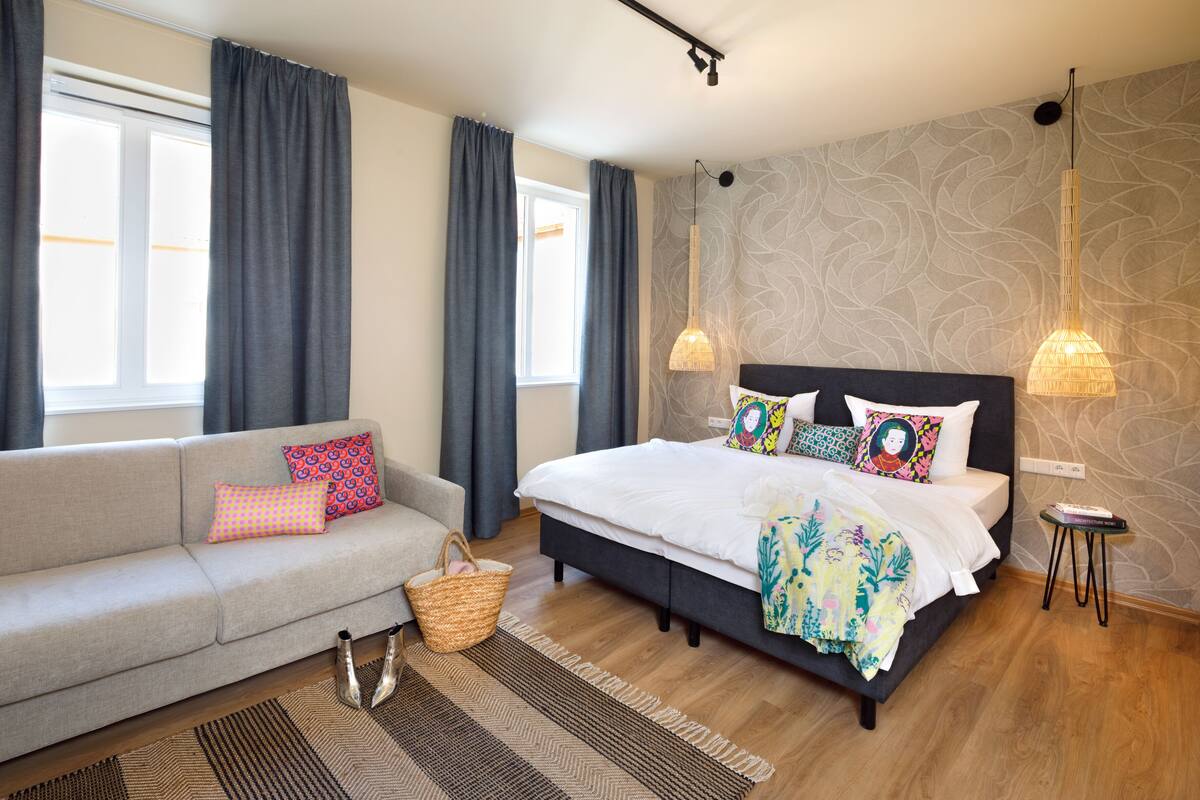 Un dormitorio con cama, sofá, lámpara colgante y una mesita.