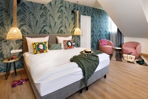 A bedroom with a large bed, two bedside tables, a chair, and a small table with a lamp. - Hotel Das Regensburg (Regensburg)