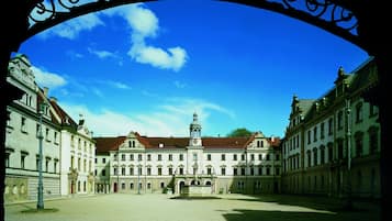 A spacious courtyard with classical architecture, a central fountain, and a clear blue sky.