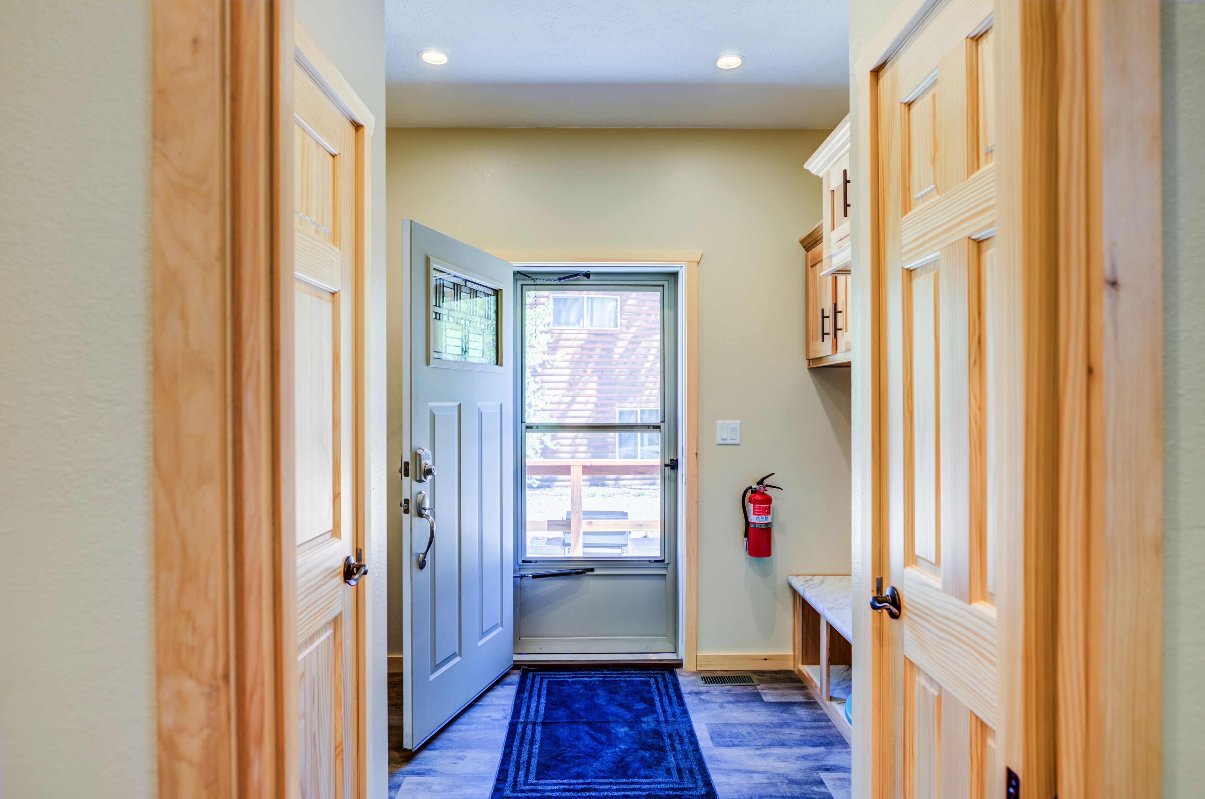 Un couloir avec des portes en bois, un tapis bleu et un extincteur accroché au mur.