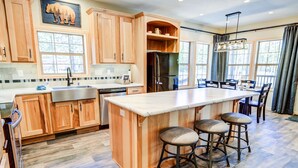 A kitchen with wooden cabinets, a stainless steel refrigerator, a large island with stools, and a dining area with chairs.