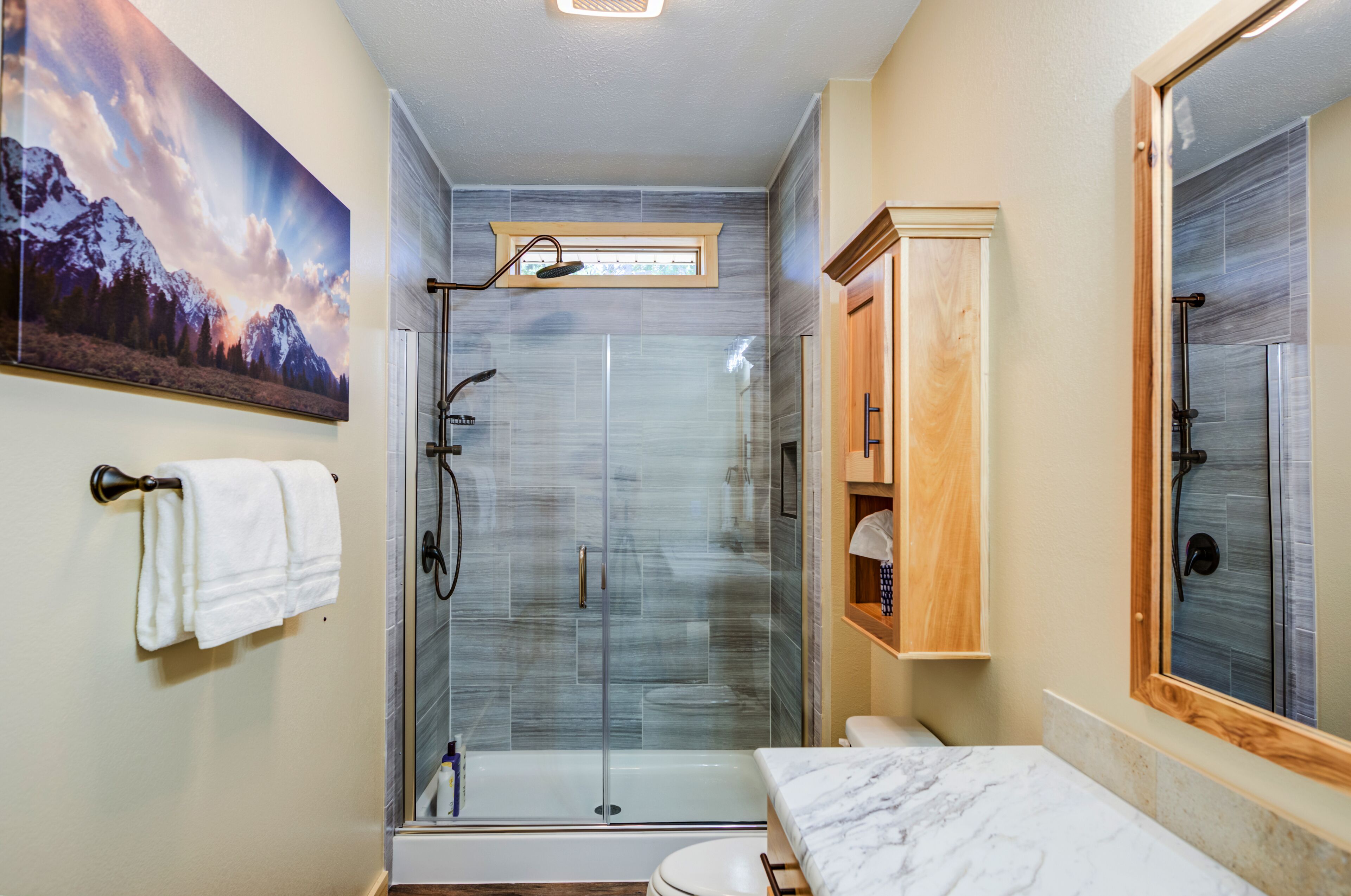 A bathroom with a glass-enclosed shower, a toilet, a sink with a marble countertop, and a wooden cabinet.