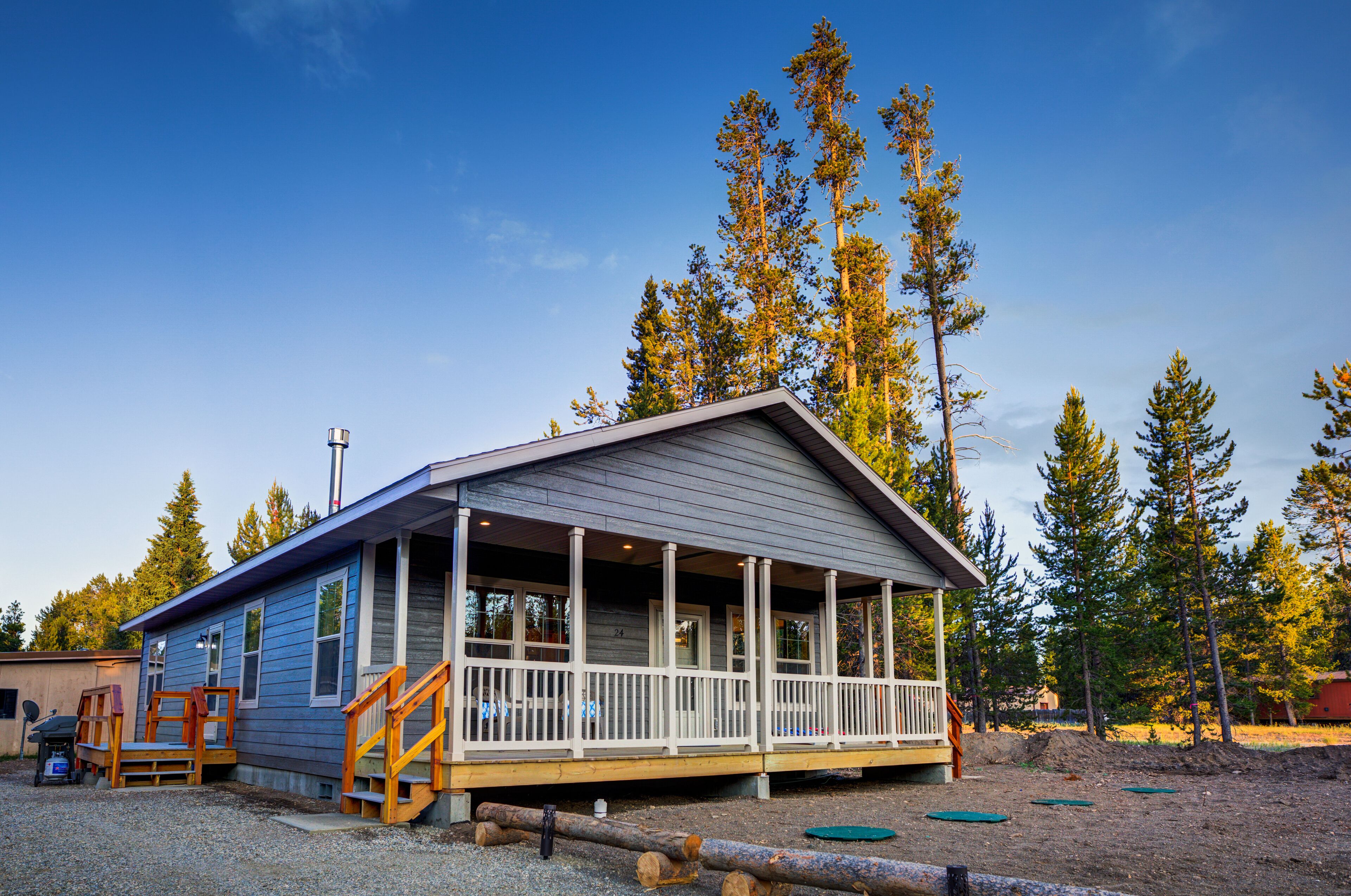 Une petite cabane à un seul étage, dotée d’un porche et entourée de grands pins.