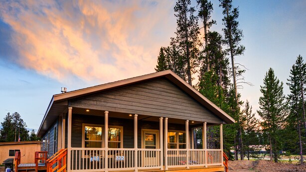 A cabin with a wooden deck and a porch, surrounded by tall pine trees.