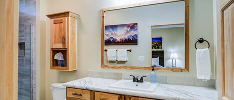 A bathroom with a marble sink, wooden cabinets, a large mirror, and a shower enclosure.