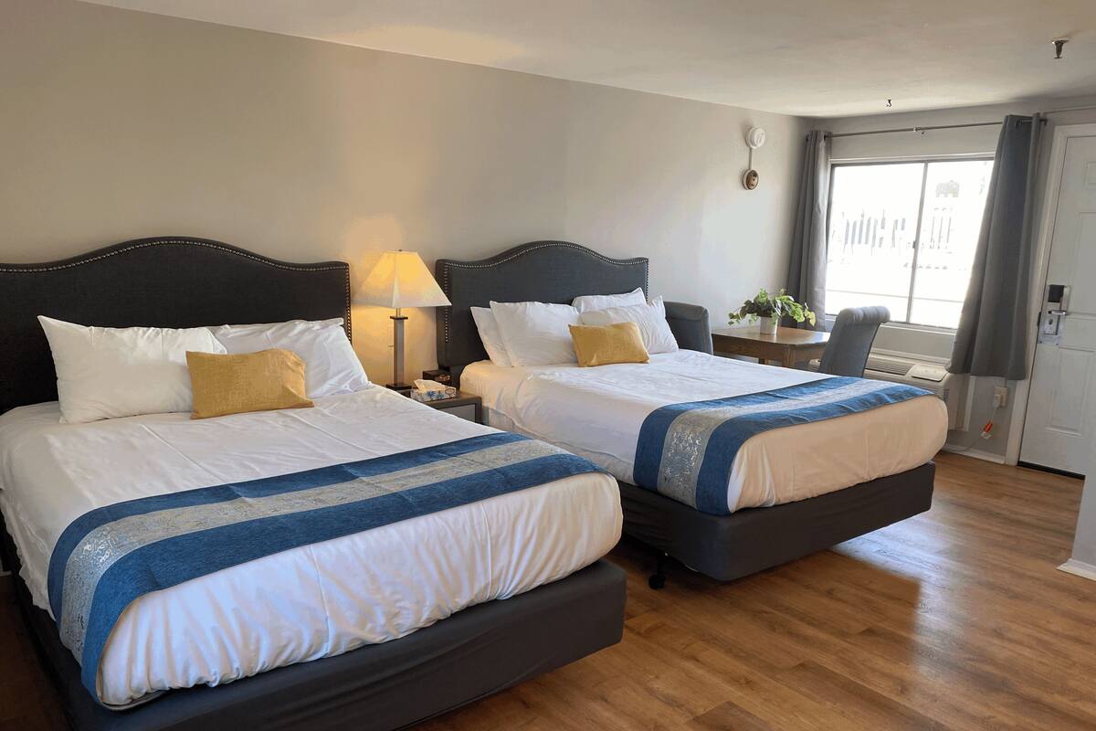 A hotel room with two beds, a desk, a chair, and a window with curtains.