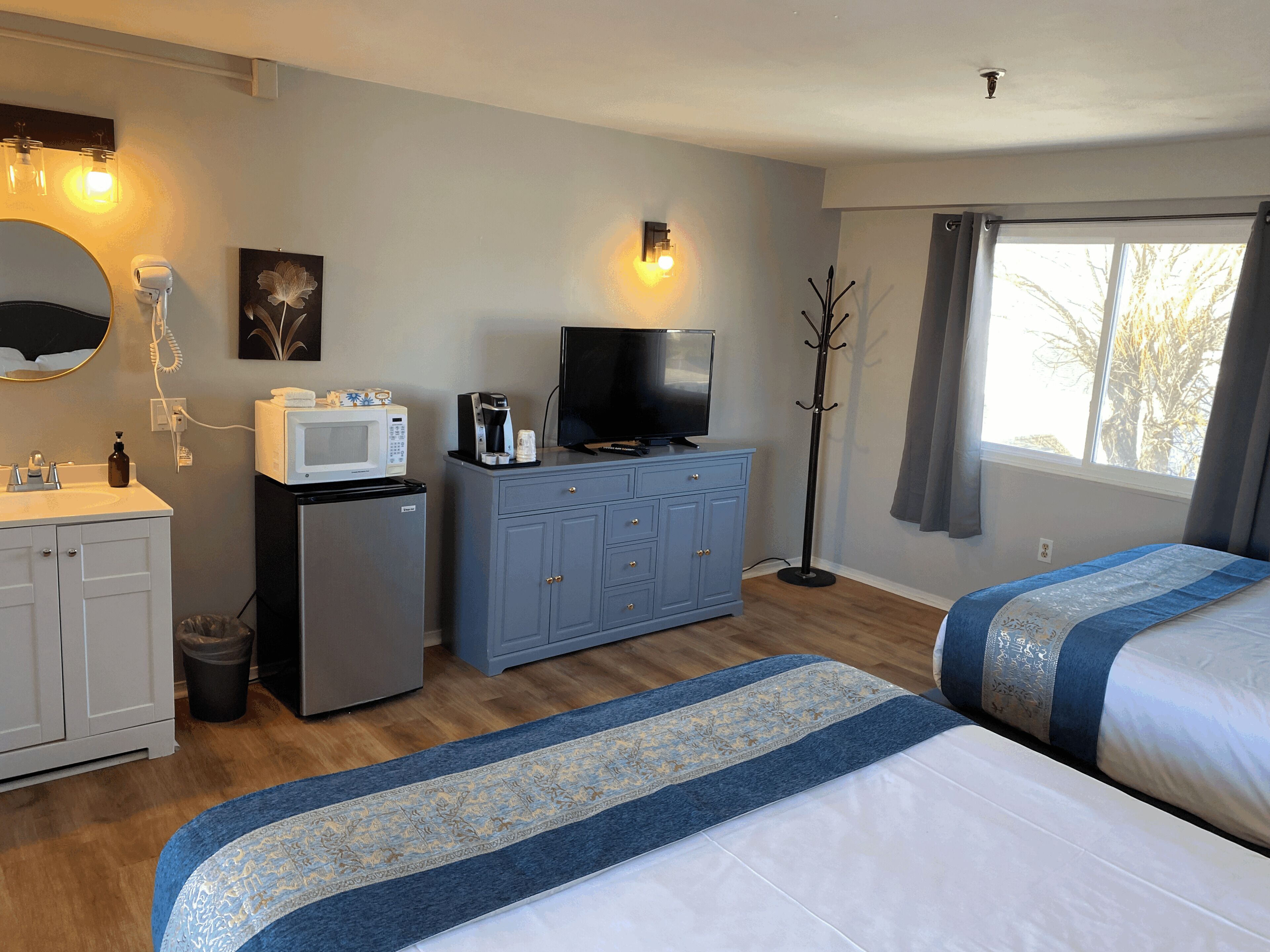 Ein Hotelzimmer mit einem Bett, einem Schreibtisch mit Computer, einer Mikrowelle, einer Kaffeemaschine, einem Fernseher und einem Fenster mit Vorhängen.