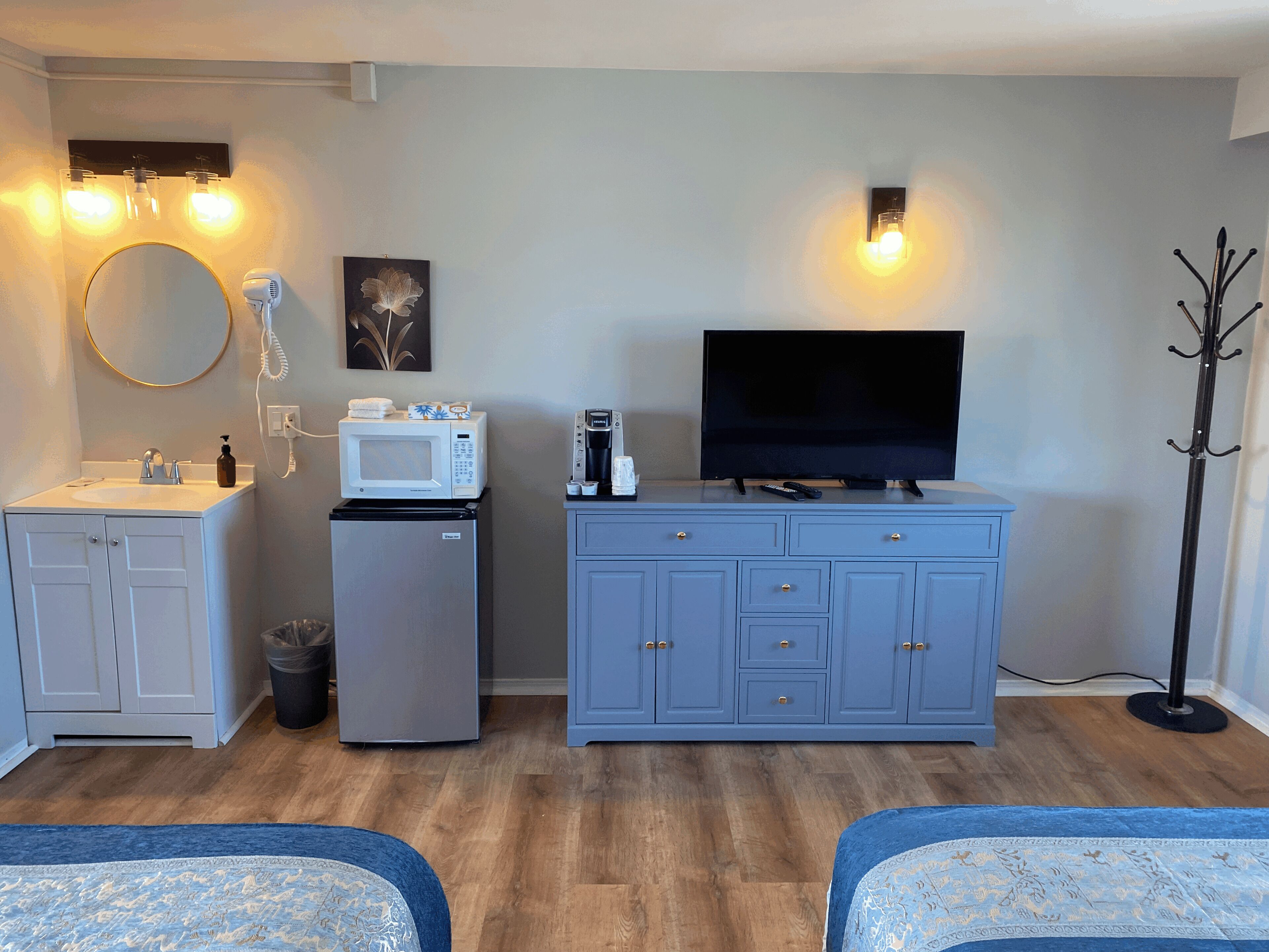Een compacte kamer met kitchenette, een flatscreen televisie, een kapstok en een kleine koelkast.