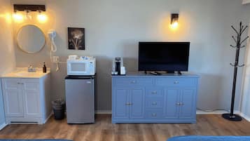 Een compacte kamer met kitchenette, een flatscreen televisie, een kapstok en een kleine koelkast.