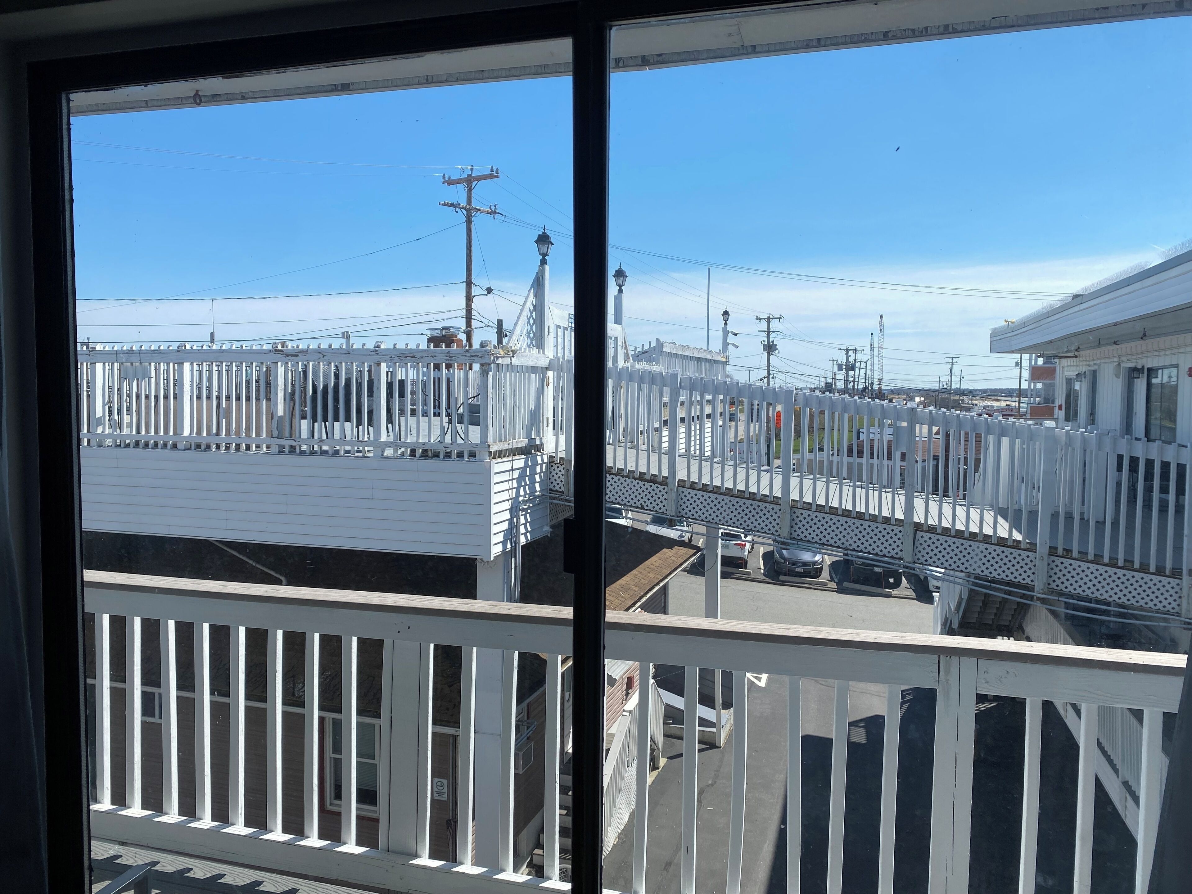Blick von einem Balkon mit weißen Geländern auf einen eingezäunten Bereich mit Gebäuden und einer Straße.