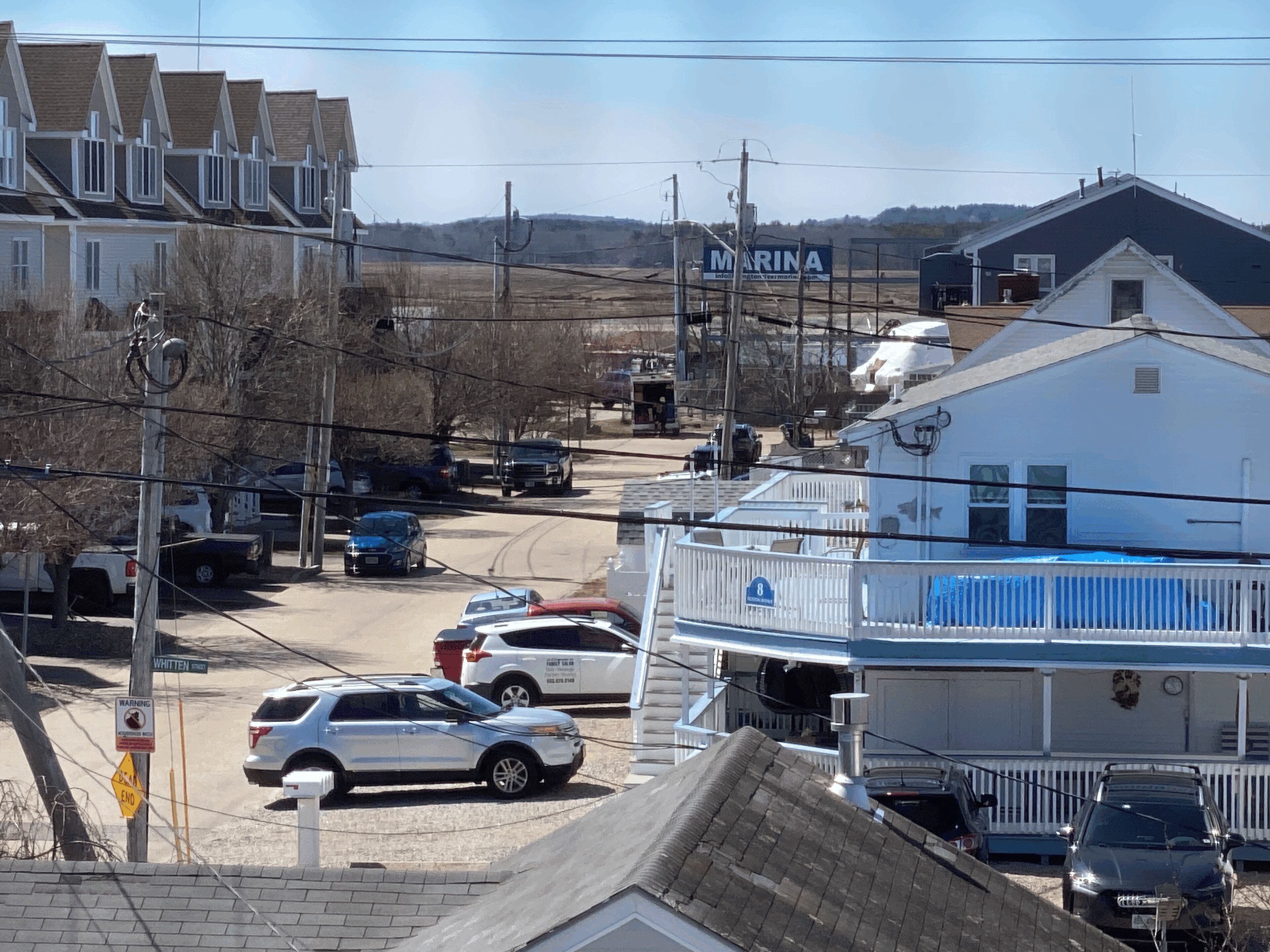 A coastal town with a marina, a row of houses, and parked cars along a street.