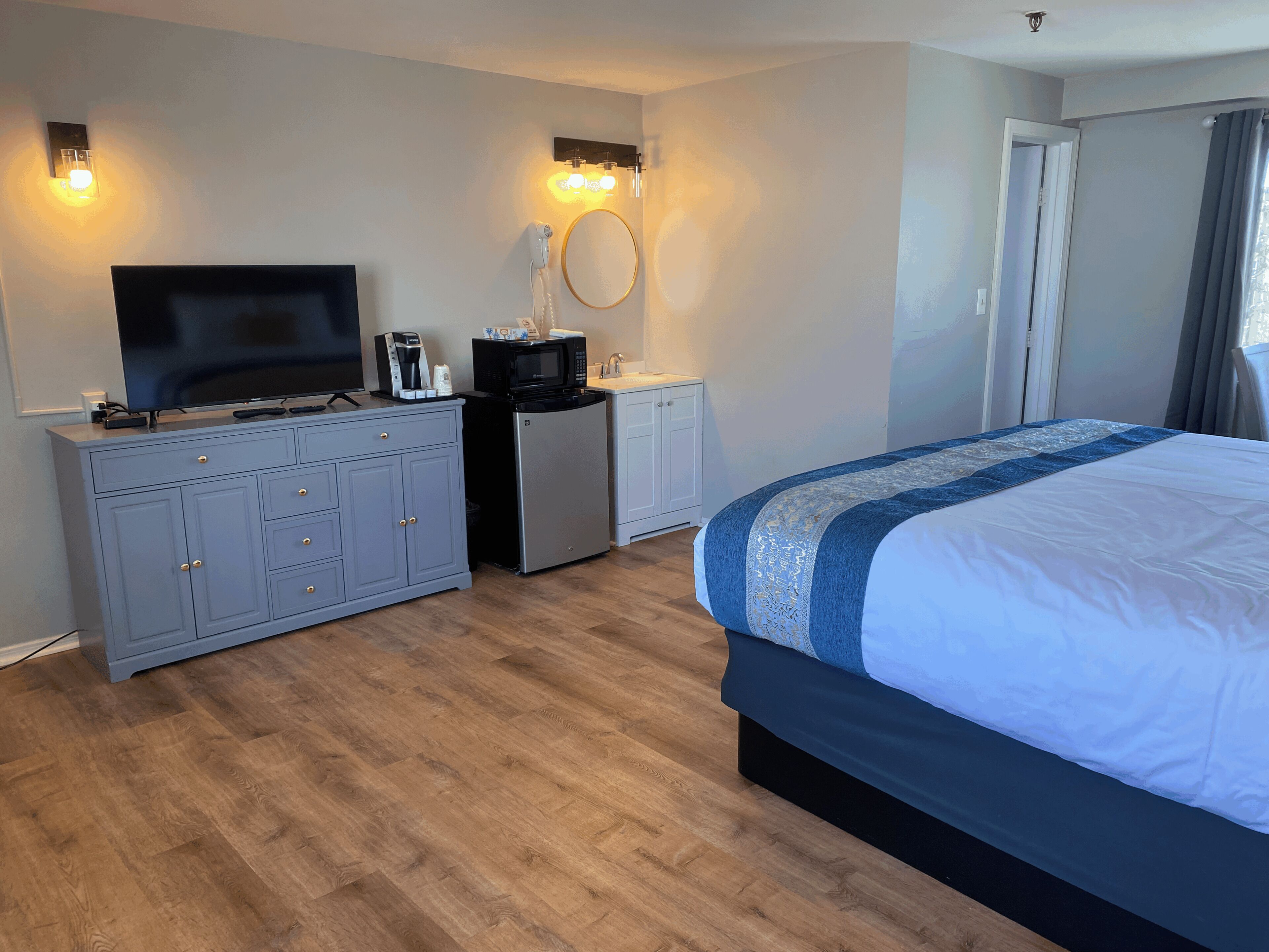 Una habitación de hotel con cama, televisión, minibar, espejo y puerta.