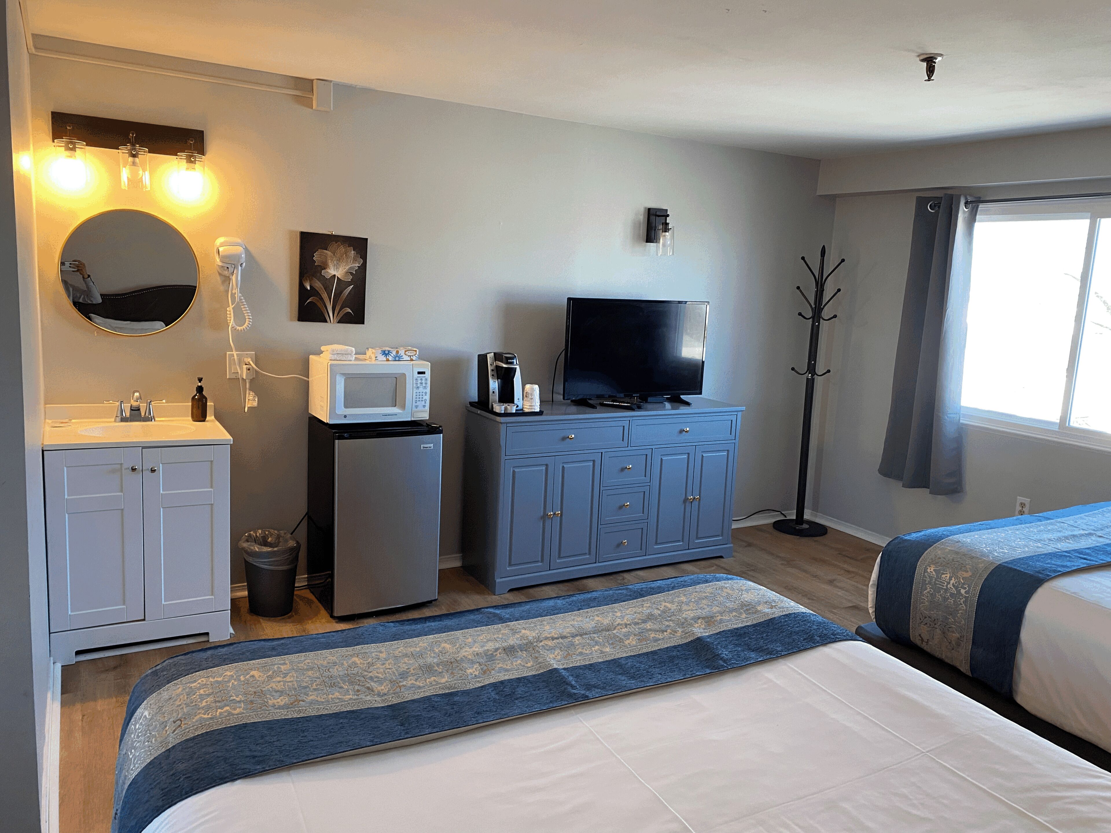 A hotel room with a bed, a TV, a minibar, a small fridge, a sink, and a mirror.